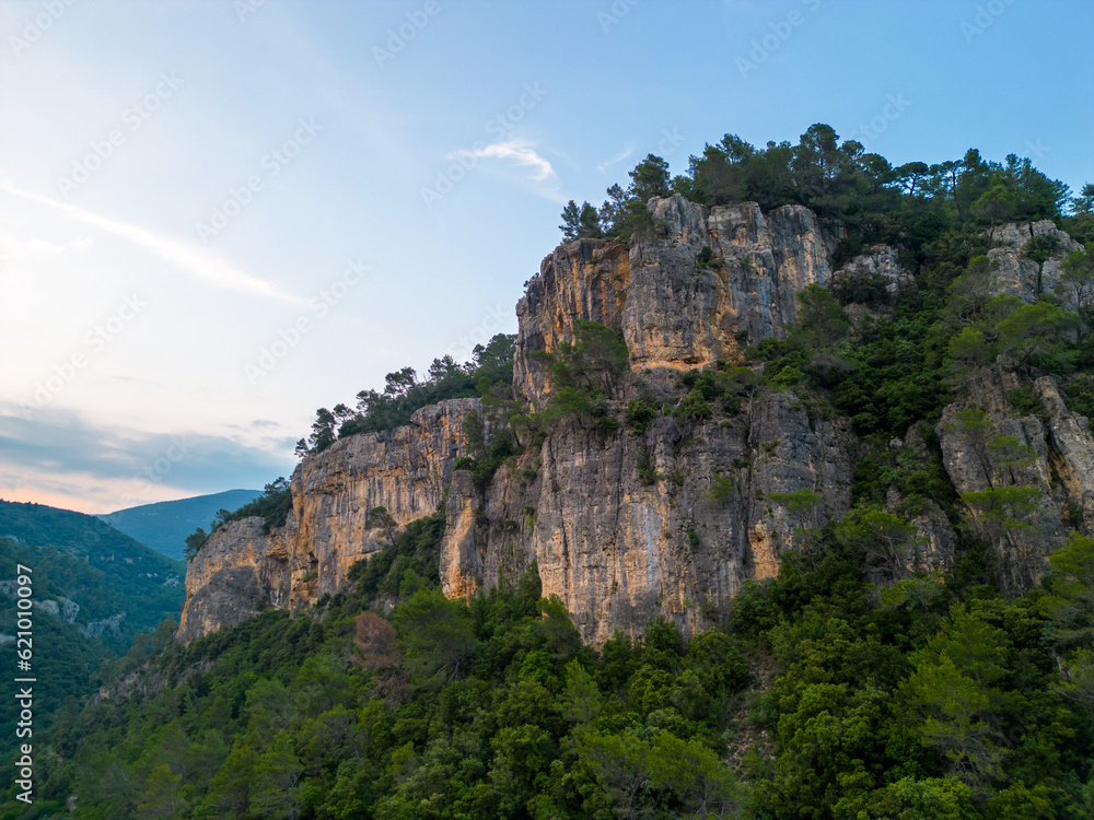 Steep rocky cliffs over forested landscape at golden hour