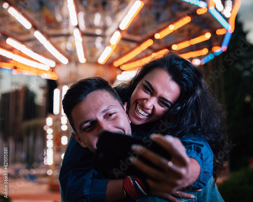Bild auf Leinwand Young happy couple taking selfie while having fun at night in an amusement park