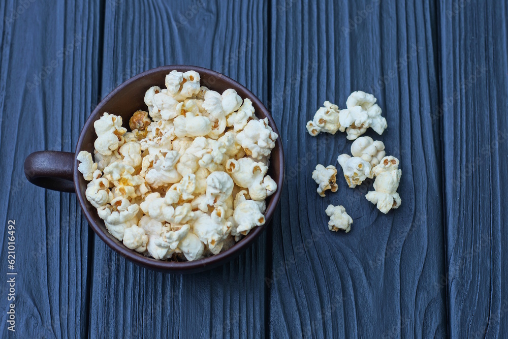 food from a pile of white popcorn in a brown cup on a black wooden table food from a pile of white popcorn in a brown cup on a black wooden table