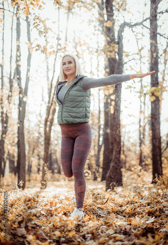 Young athletic woman with perfect body practices leg stretching before workout in autumn forest. Outdoor workout