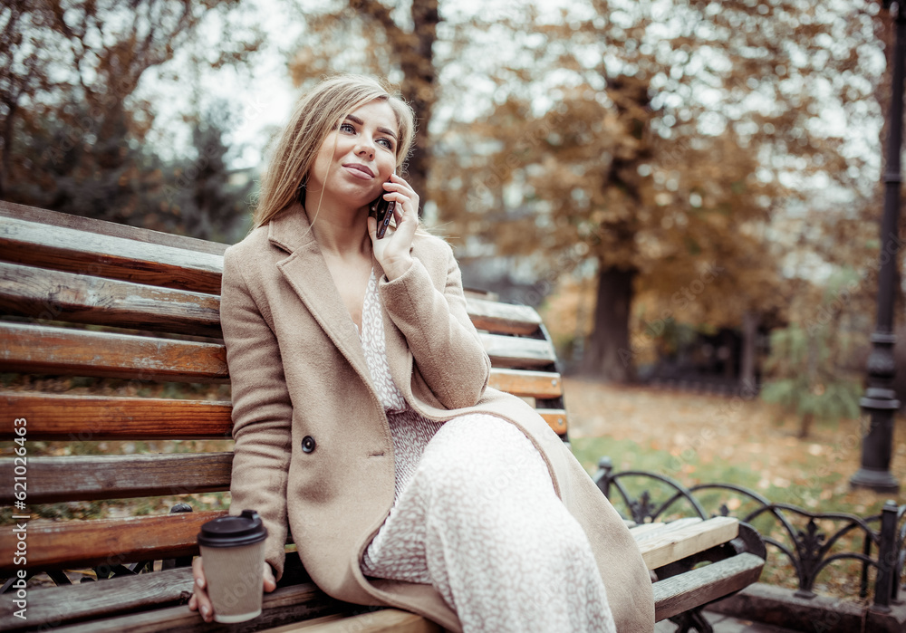 Cute beautiful woman talking on the phone while sitting on a bench in the autumn park Cute beautiful woman talking on the phone while sitting on a bench in the autumn park