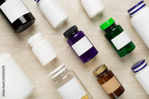 Plastic bottles with vitamins on wooden background, top view