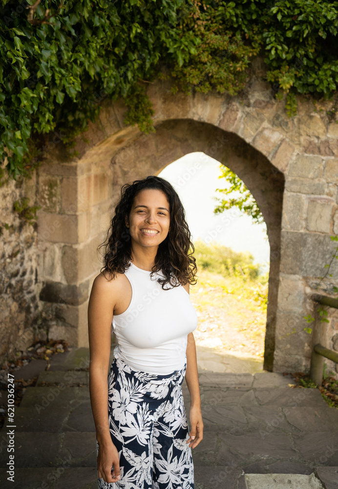 Young hispanic woman smiling in front of an archway with vegetation Young hispanic woman smiling in front of an archway with vegetation
