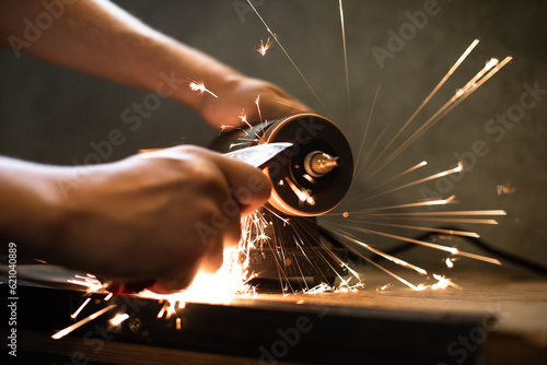 Close-up of men's hands sharpening an axe on an electric sharpener. Repair of home tools. 
Sparks fly.