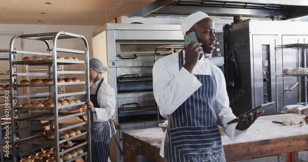 Diverse bakers in bakery kitchen, talking on smartphone and holding bakery sheets in slow motion Diverse bakers in bakery kitchen, talking on smartphone and holding bakery sheets in slow motion
