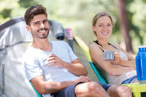 couple having a drink from thermos by their tent