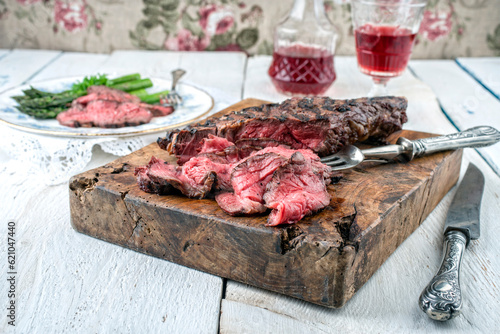 Traditional wagyu entrecote beef steak with green asparagus and red wine served on an old rustic wooden board