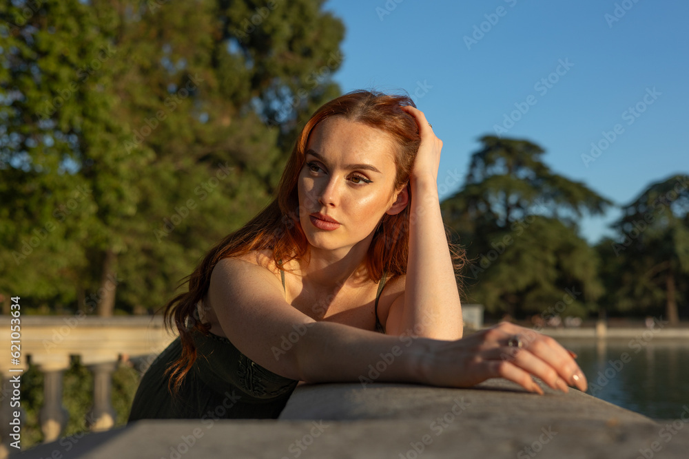 very beautiful freckled white woman with long red hair leaning on the railing and her back to the lake and trees with the sun reflecting on her face very beautiful freckled white woman with long red hair leaning on the railing and her back to the lake and trees with the sun reflecting on her face