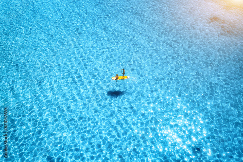 Aerial view of with man and woman on sup board in blue sea at sunset in summer. People on floating canoe in transparent water. Kayak. Sardinia island, Italy. Tropical seascape. Active travel. Top view