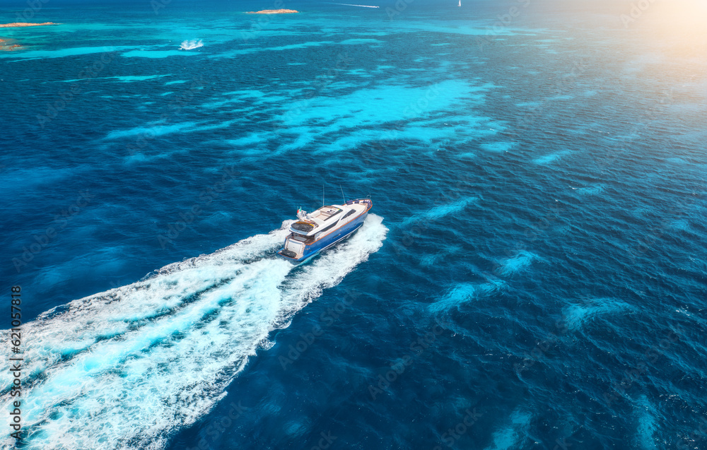 Obraz premium Aerial view of fast floating yacht on blue sea at sunny day in summer. Travel in Sardinia, Italy. Aerial view of speed boat, sea lagoon, transparent azure water. Top drone view. Tropical seascape