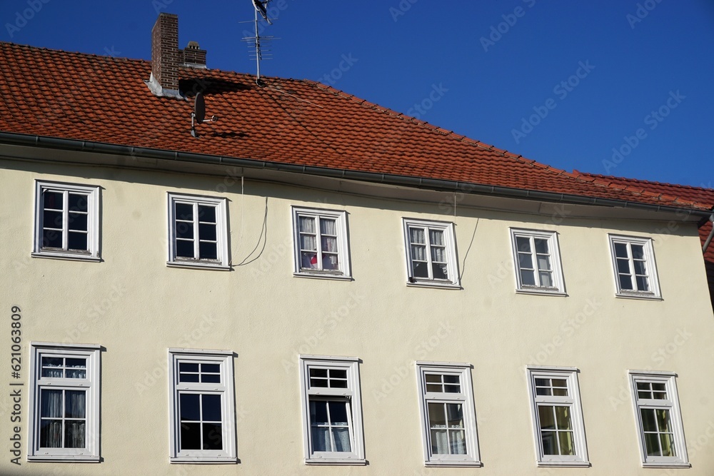 Großes altes saniertes Wohnhaus mit weißer Fassade und Fenstern mit weißen Rahmen und altem roten Ziegeldach vor blauem Himmel bei Sonne am Nachmittag im Sommer
