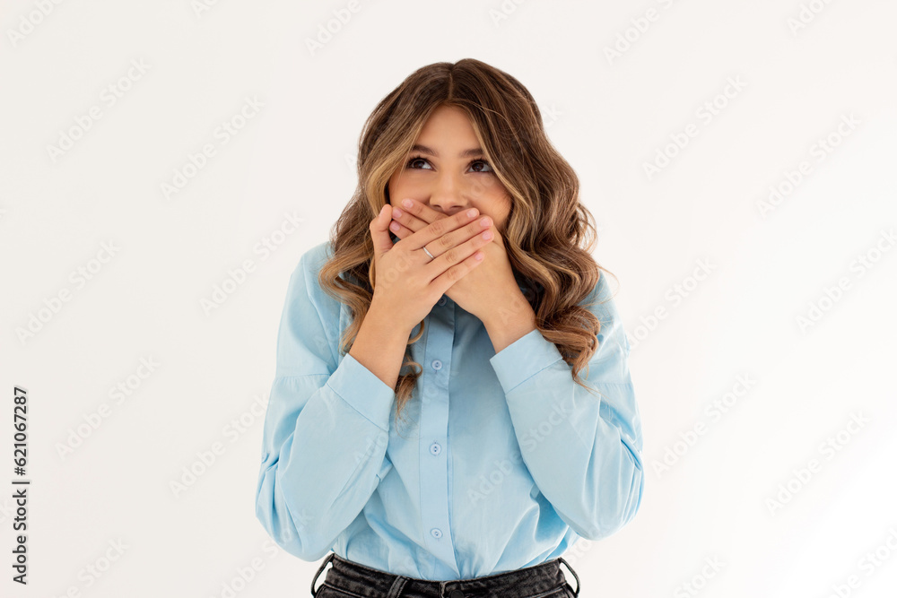 Young laughing pretty girl woman covers mouth with hands tries to hide joy or laughter after hearing joke dressed in blue shirt stands in white background Young laughing pretty girl woman covers mouth with hands tries to hide joy or laughter after hearing joke dressed in blue shirt stands in white background