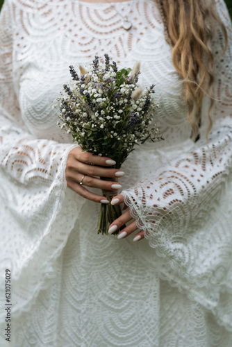Bride in white boho dress with wedding bouquet. Woman hands holding bunch of Gypsoghila flowers.