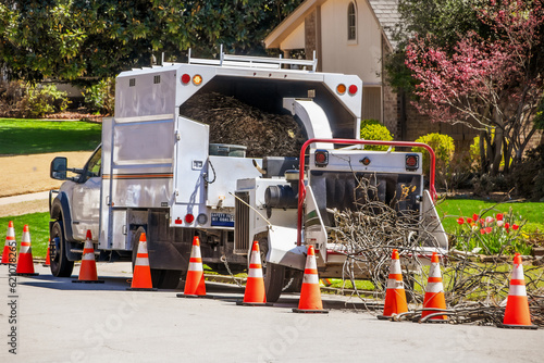 Utility Panel truck with attached wood chipper grinding up branches in nice neighborhood with safety cones