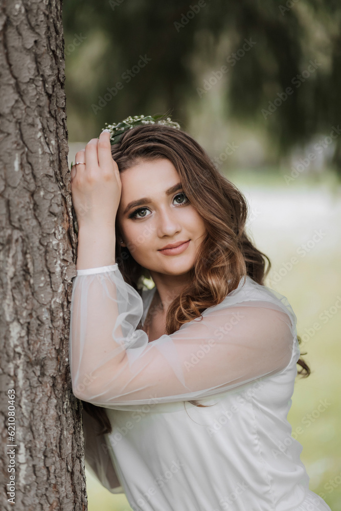 Portrait of a girl with long hair and a wreath on her head near a tall tree Portrait of a girl with long hair and a wreath on her head near a tall tree