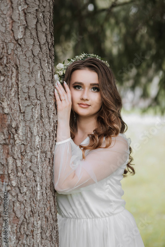 Portrait of a girl with long hair and a wreath on her head near a tall tree