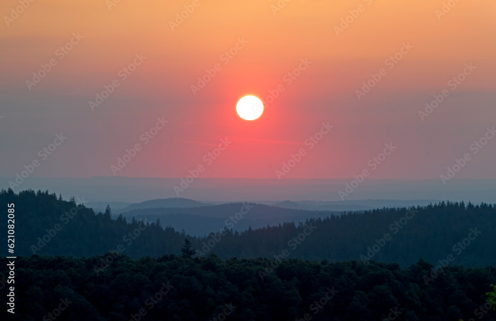 Sunset over de hills of the Vosges, an orange colored sun in the evening sky, hill ranges fading in the distance