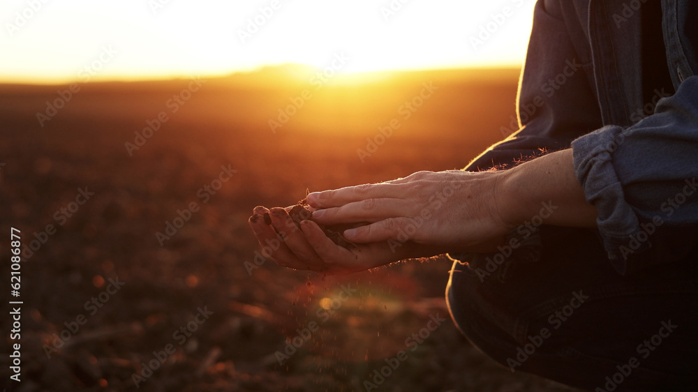 Male farmer's hand holds a handful of dry ground and checks soil fertility and quality before sowing crops on plowed field at sunset. Cultivated land. Concept of organic agriculture and agribusiness Male farmer's hand holds a handful of dry ground and checks soil fertility and quality before sowing crops on plowed field at sunset. Cultivated land. Concept of organic agriculture and agribusiness