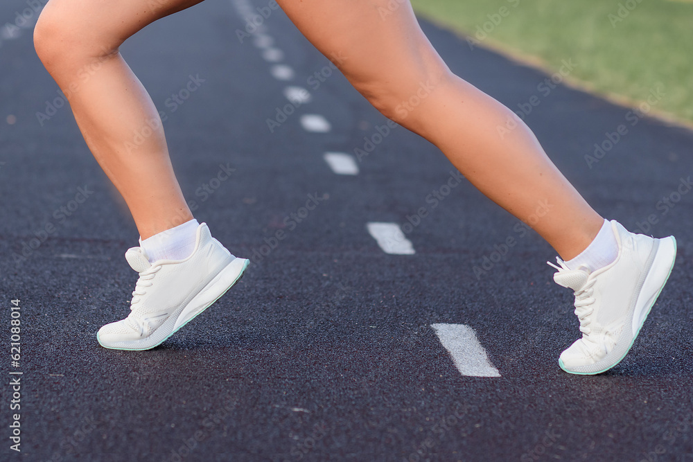 legs girl in a sports blue T-shirt and shorts goes in for sports at the stadium. Girl running in the stadium