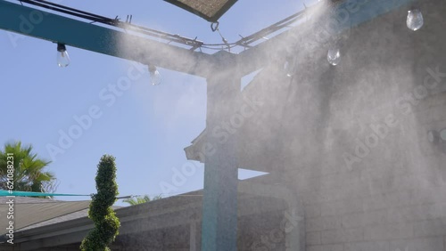 This video shows misters giving off water in slow motion, against a blue sky background. 