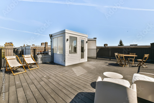 a deck with two chairs and a table on the left side of the deck, there is a blue sky in the background