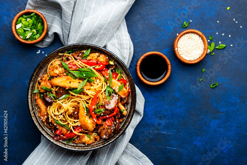 Stir fry egg noodles with chicken, paprika, mushrooms, chives and sesame seeds in ceramic bowl. Asian cuisine dish. Blue stone table background, top view