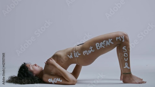 Hispanic woman with body pain lifts her bare body off the ground on a white backdrop