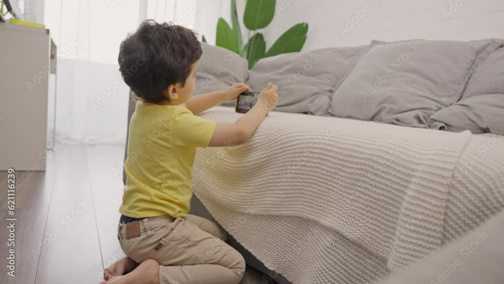 Adorable small child sitting on floor playing with smartphone on sofa at home Adorable small child sitting on floor playing with smartphone on sofa at home