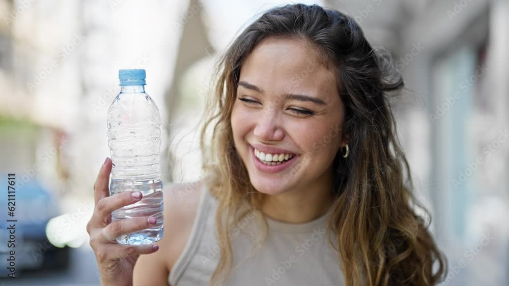 Young beautiful hispanic woman holding bottle of water smiling at street Young beautiful hispanic woman holding bottle of water smiling at street