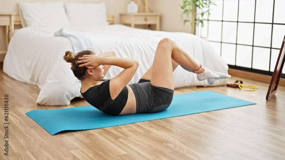 Young beautiful hispanic woman training abs exercise at bedroom