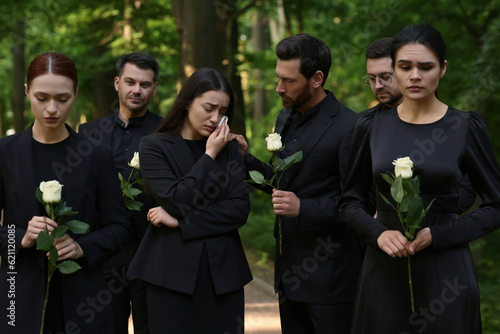 Funeral ceremony. Sad people with white rose flowers mourning outdoors