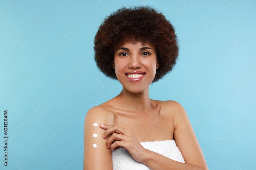 Beautiful young woman applying body cream onto arm on light blue background Beautiful young woman applying body cream onto arm on light blue background