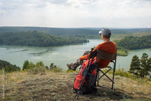 man sitting on a camp chair on top of mountain resting after hiking and  looking in the mountains.