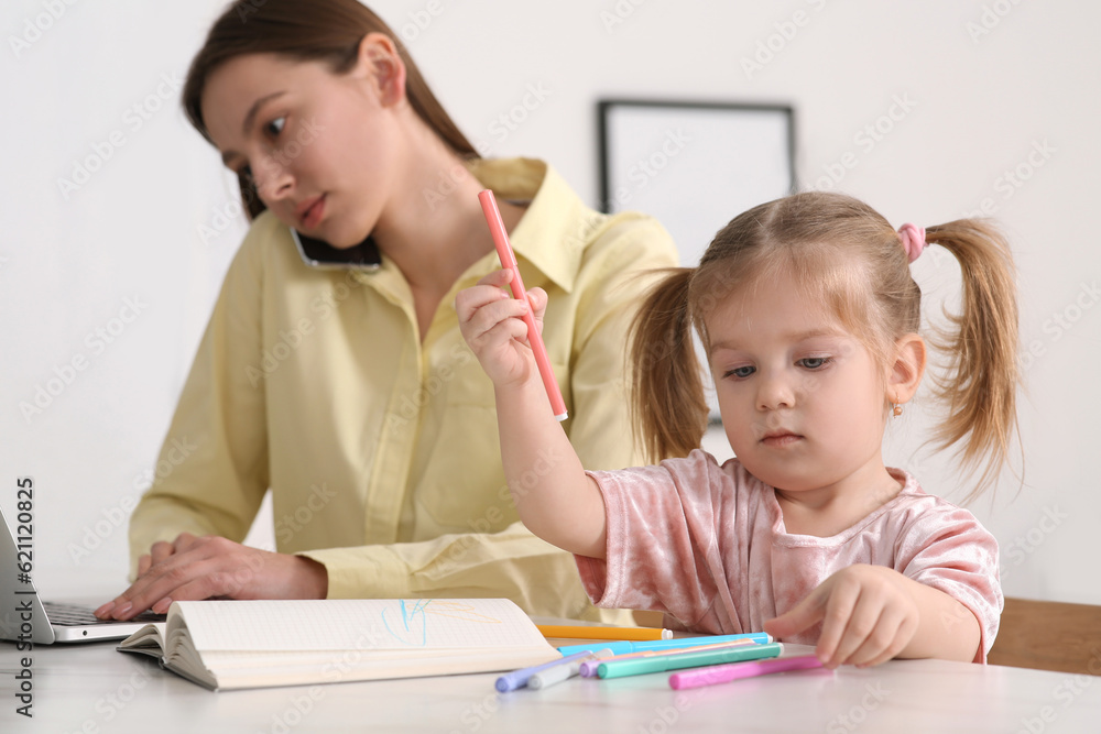 Woman with laptop working remotely at home. Busy mother talking on phone while her daughter drawing at desk. Selective focus Woman with laptop working remotely at home. Busy mother talking on phone while her daughter drawing at desk. Selective focus