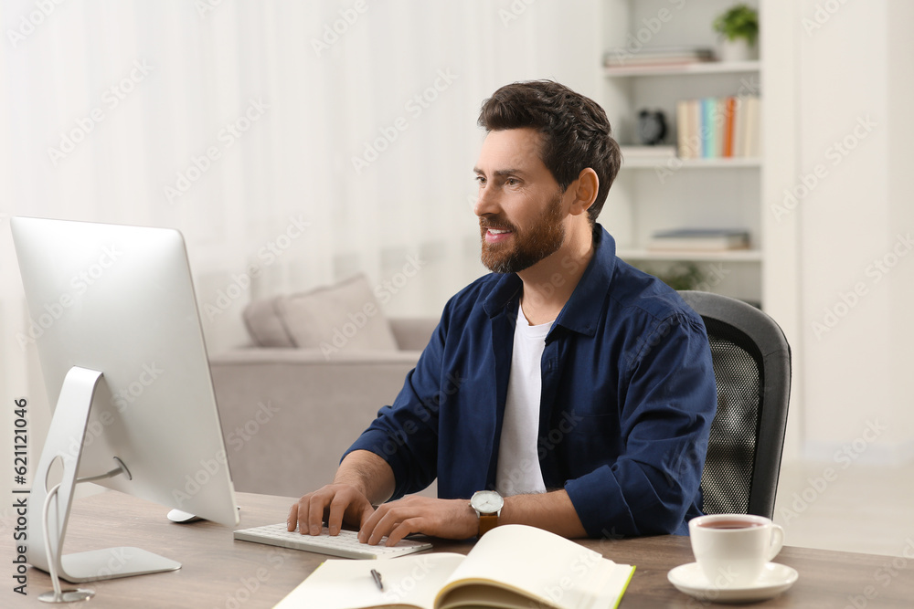 Fototapeta premium Home workplace. Happy man working with computer at wooden desk in room
