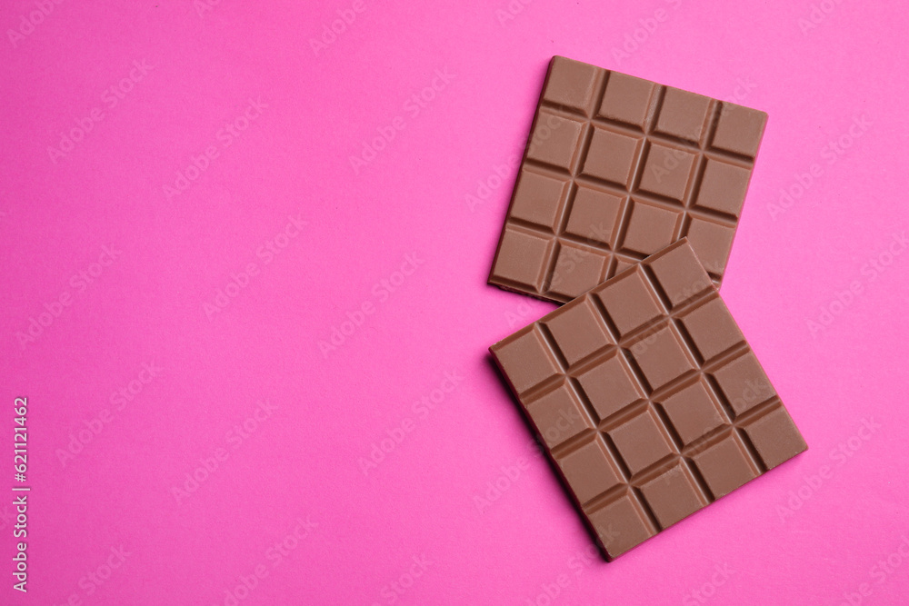 Fototapeta premium Pieces of tasty milk chocolate bar on pink background, flat lay. Space for text