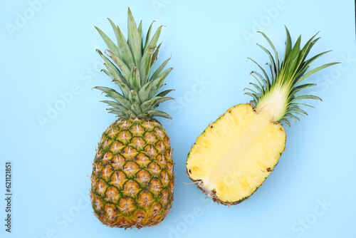 Whole and cut ripe pineapples on light blue background, flat lay