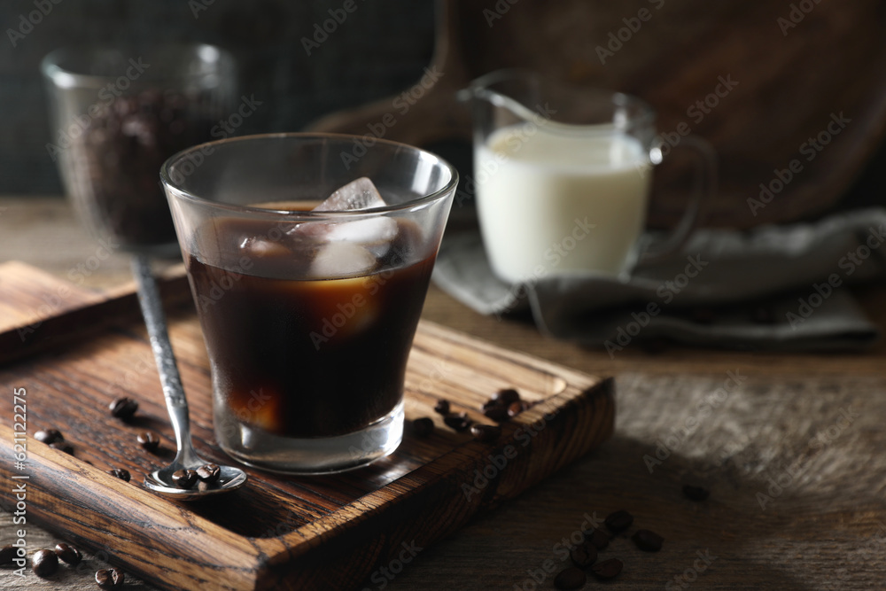 Glass of delicious iced coffee and beans on wooden table, space for text Glass of delicious iced coffee and beans on wooden table, space for text