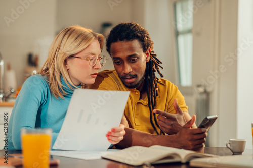Fotografia, Obraz A serious interracial couple is planning a budget and doing home finances together in their cozy home