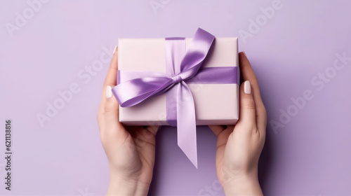 Female hands holding a purple gift box with a bow. © tashechka