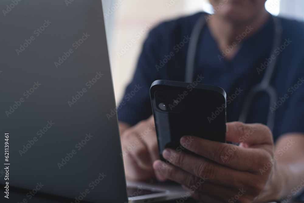 Doctor using mobile smart phone, working on laptop computer in medical workspace office with stethoscope on desk, close up, teleconference, telemedicine, medical research and technology concept Doctor using mobile smart phone, working on laptop computer in medical workspace office with stethoscope on desk, close up, teleconference, telemedicine, medical research and technology concept