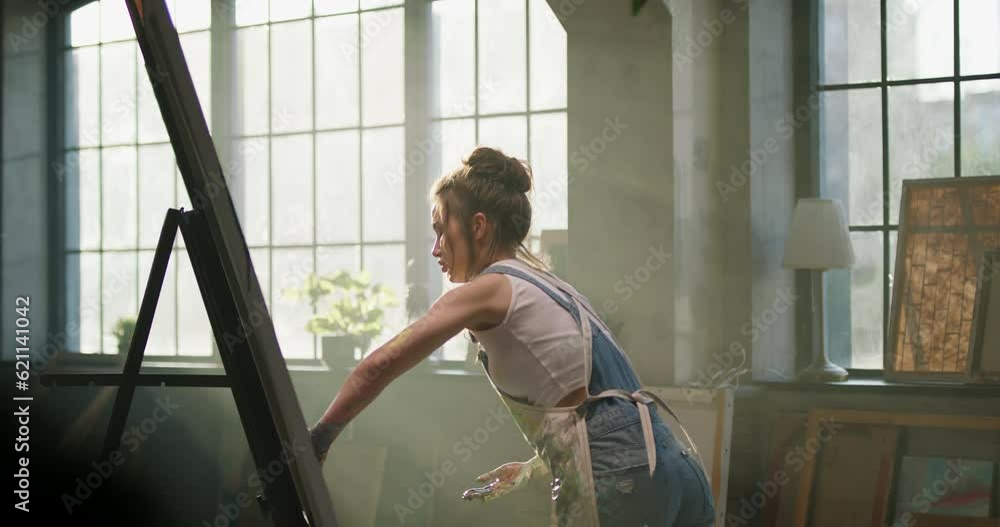 Millennial girl artist paints picture in loft studio puts paint on canvas with her hands. Cinematic. Women's power, she creates colorful, emotional, sensual painting. Beautiful female hands, sun rays Millennial girl artist paints picture in loft studio puts paint on canvas with her hands. Cinematic. Women's power, she creates colorful, emotional, sensual painting. Beautiful female hands, sun rays