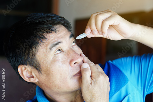 Asian man uses artificial tear lubricant eye drops with his eyes. Concept, Healthcare. Treatment for dry eye symptoms, eye inflammation diseases. Relief irritated optics. 