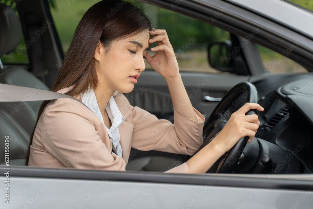 Closed eyes tired young Asian woman with headache sitting in her parked car behind the wheel with seatbelt fasten while holding her hand over her forehead to ease the pain Closed eyes tired young Asian woman with headache sitting in her parked car behind the wheel with seatbelt fasten while holding her hand over her forehead to ease the pain