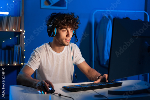 Young arabic gamer wearing headphones playing video game on personal computer, play in eSport cyber games tournament in neon light © mtrlin