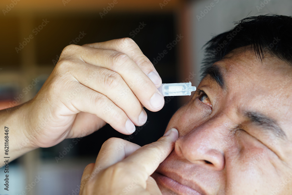 Asian man uses artificial tear lubricant eye drops with his eyes