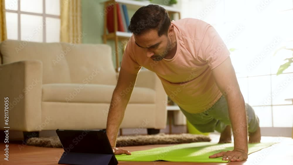 Indian man doing push ups exercise by online video classes from tablet at home - concept of Fitness instruction, Exercise Tutorial and Bodyweight Training