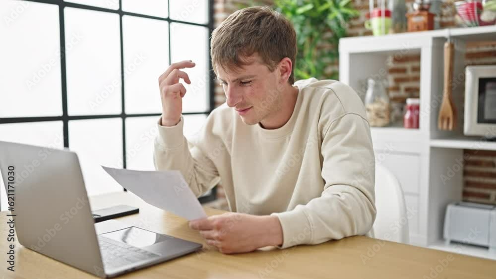 Young caucasian man using laptop reading document at dinning room Young caucasian man using laptop reading document at dinning room