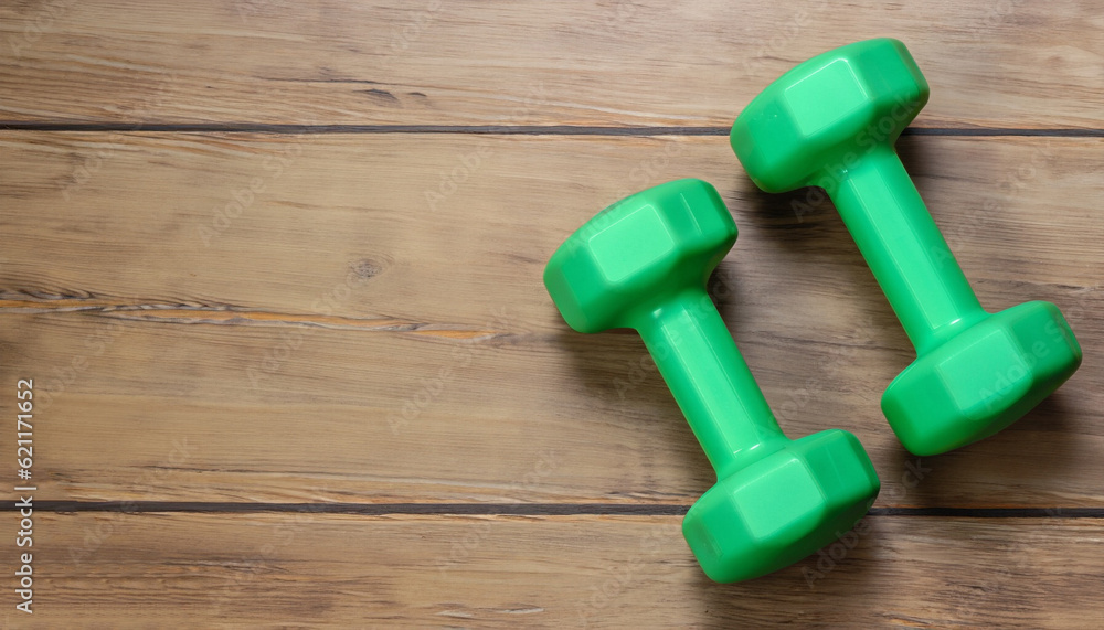 Two green dumbbells isolated on wooden background with copy space Two green dumbbells isolated on wooden background with copy space