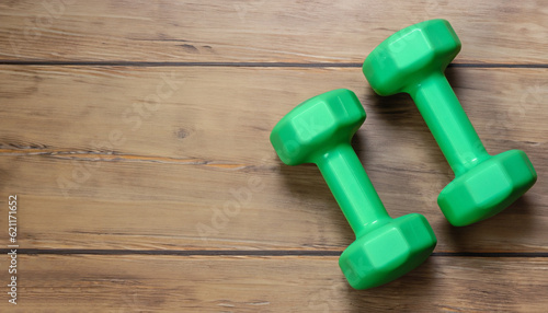 Two green dumbbells isolated on wooden background with copy space